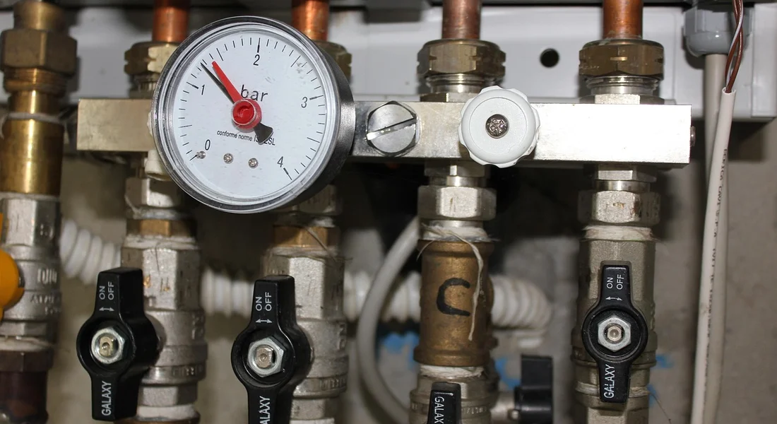 Close-up of a water heater plumbing manifold with a pressure gauge and multiple shut-off valves.