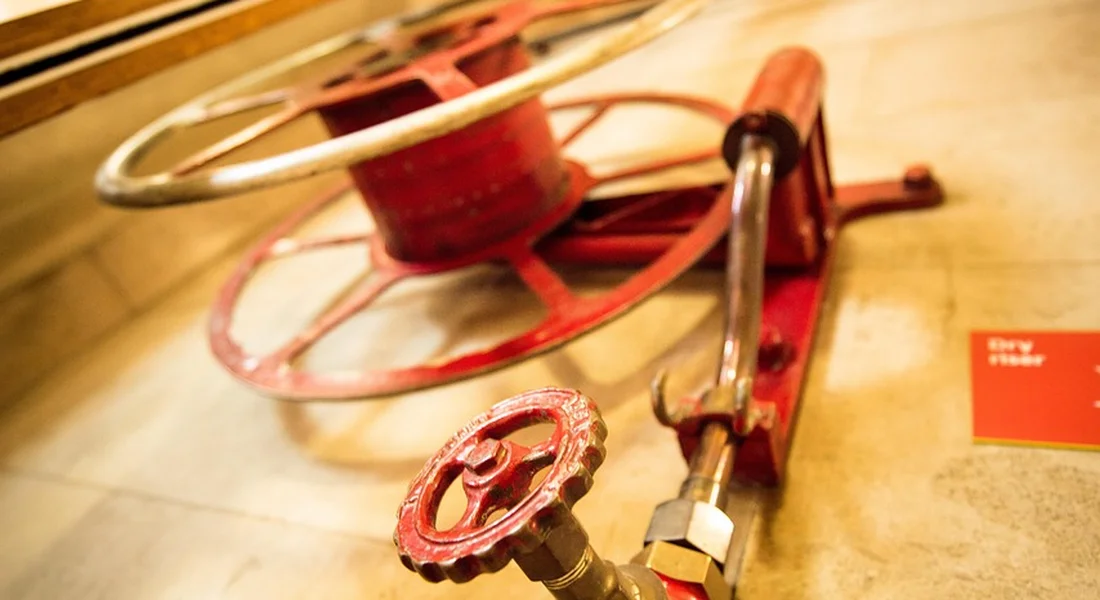 Close-up of a red valve wheel and plumbing fittings in a boiler room, representing the tools and components for installing a backflow preventer.