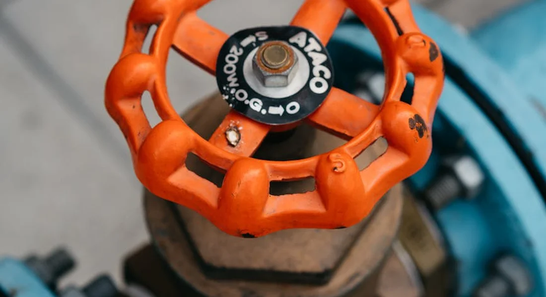 Close-up of an orange backflow valve handle on blue piping