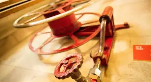 Close-up of a red plumbing valve with a wheel handle in a utility setting, illustrating installation components related to backflow prevention.