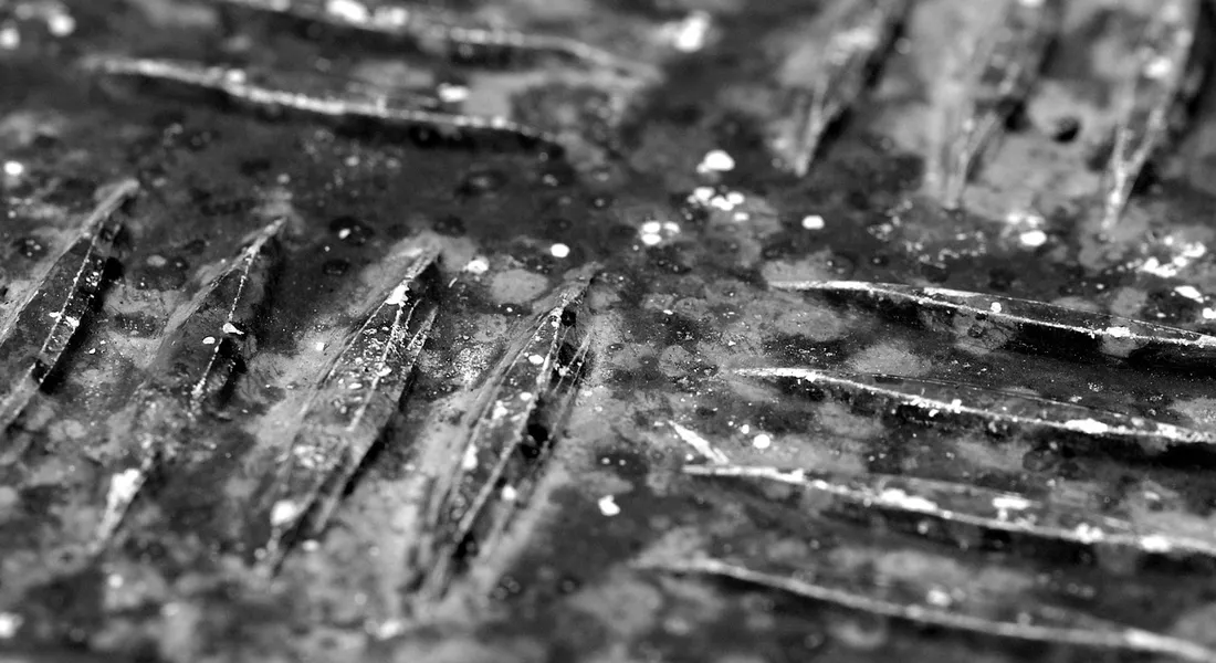 Close-up grayscale photo of a damp, ribbed surface with droplets, illustrating moisture in a drainage setting.