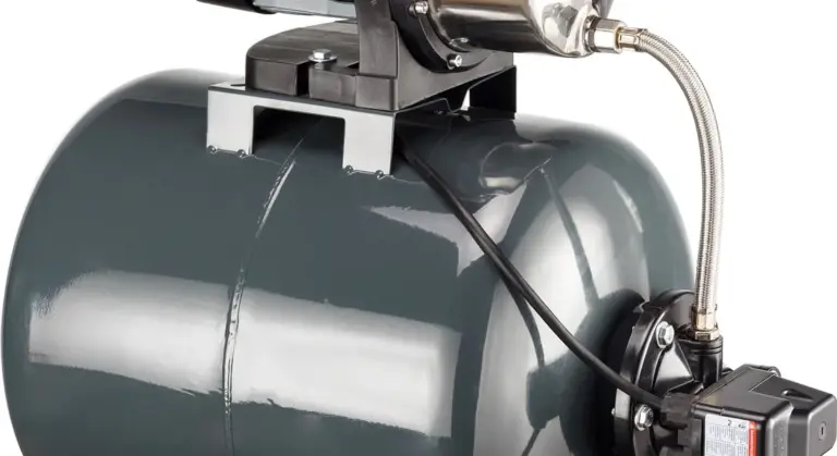 Close-up of a gray pressure tank with fittings and a discharge hose, part of a basement sump pump setup.