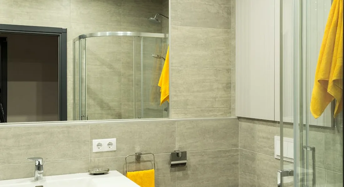 Contemporary bathroom with grey tile, a glass shower enclosure, a white sink, and a bright yellow towel.