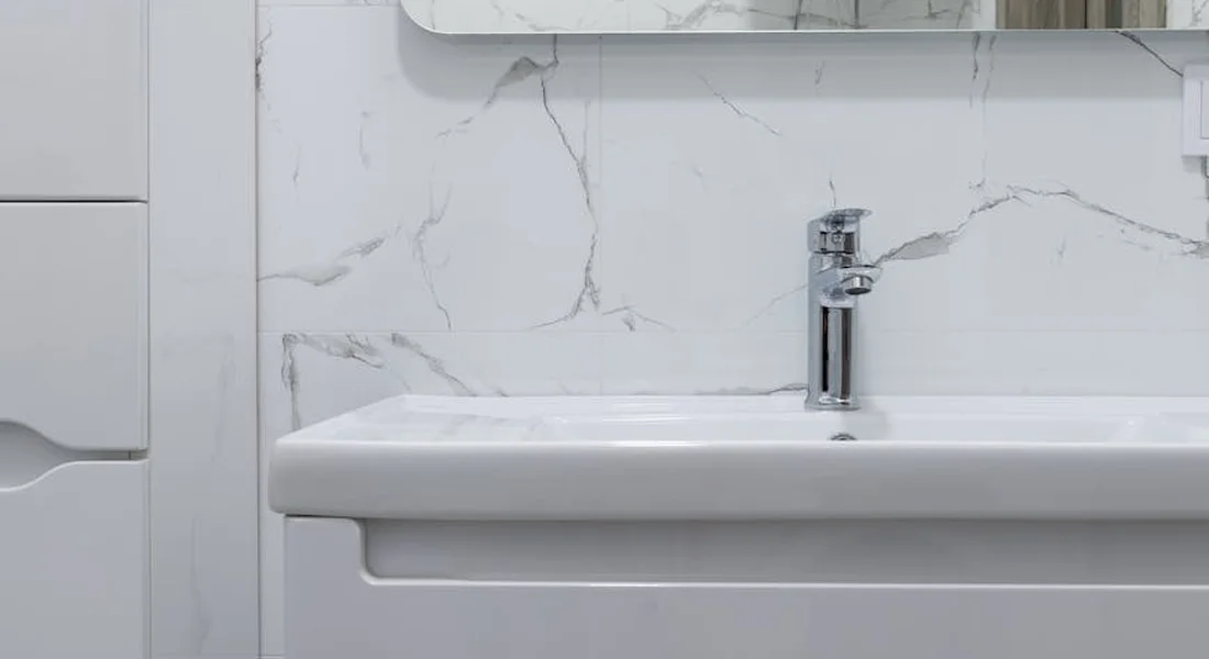 Close-up of a modern bathroom sink with a chrome faucet against a marble-tiled wall
