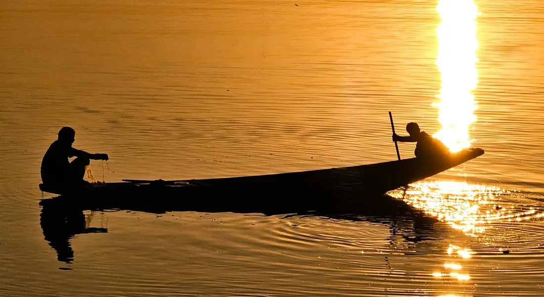 Two people in a small boat silhouetted against a sunset on calm water