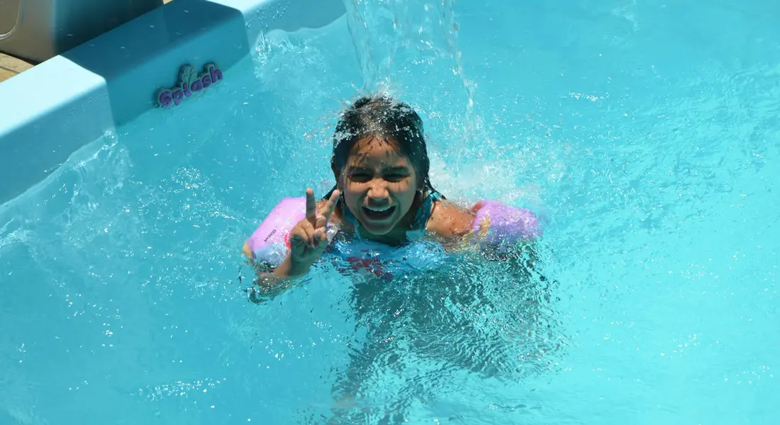 Child wearing pink arm floaties swimming in a bright blue pool
