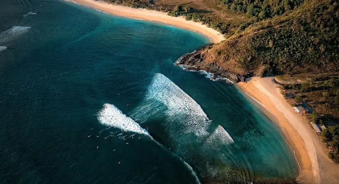 Aerial view of a coastal shoreline with turquoise water, white surf, and a sandy beach, illustrating water sampling in the field.