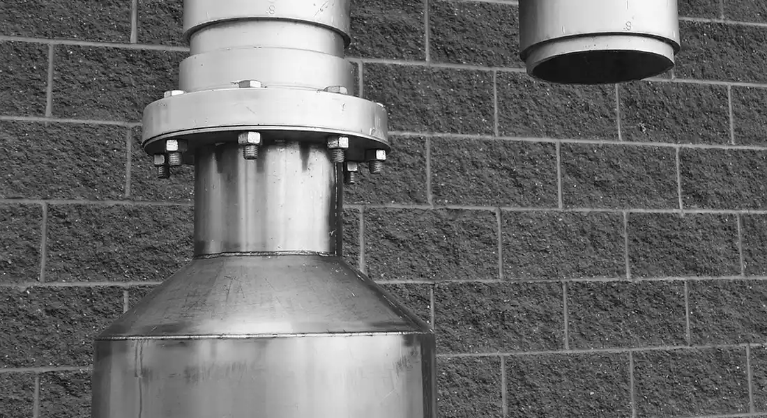 Close-up of a metal check valve assembly connected to piping mounted on a brick wall, illustrating a component of a deep well pump system.