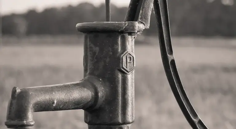 Close-up of a metal deep well pump head with piping and a power cord, shown in grayscale.