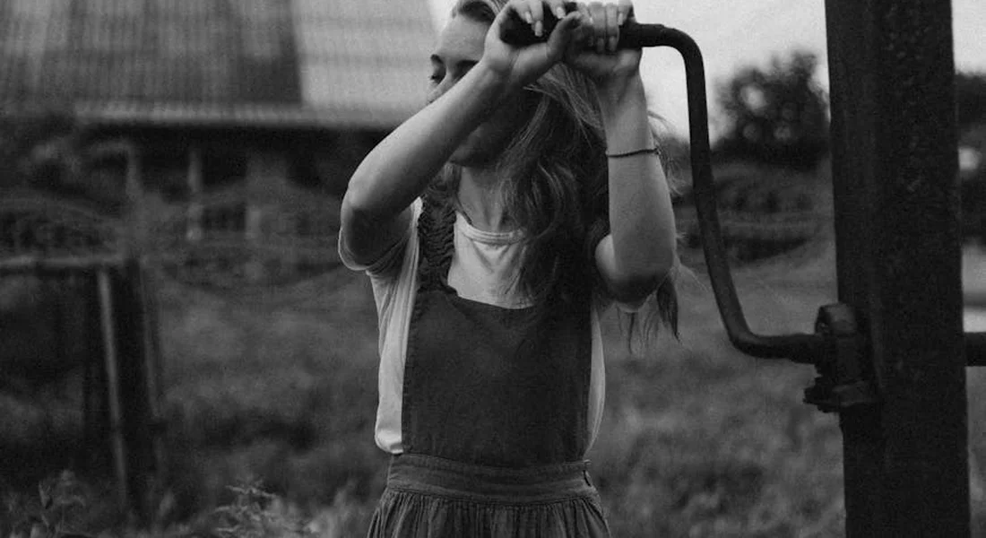 Person operating a hand water pump outdoors in a rural setting