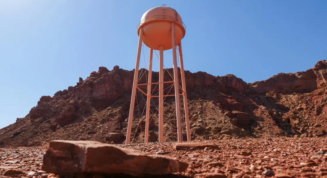 Orange water tower standing among red desert rocks under a clear blue sky.
