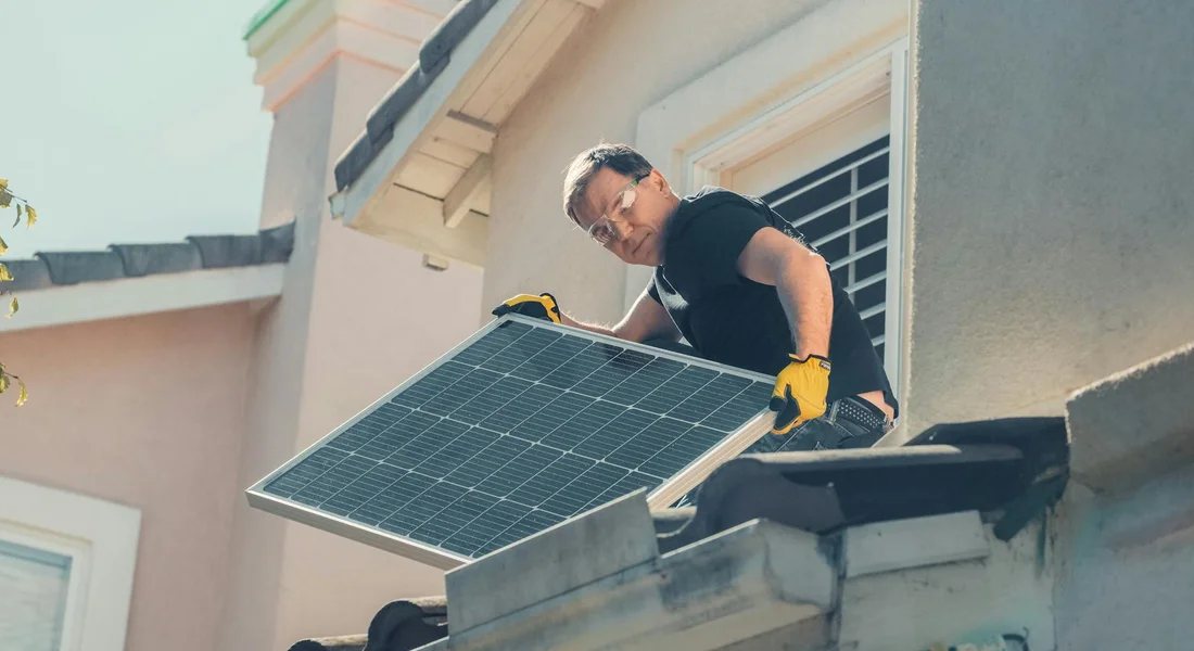 Individual wearing gloves installs a solar panel on a residential roof.