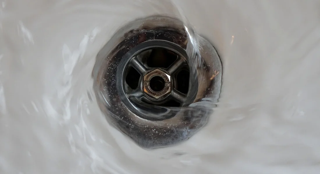 Close-up of a metal drain opening embedded in white ceramic, illustrating the drain components used in water heater drain pans.