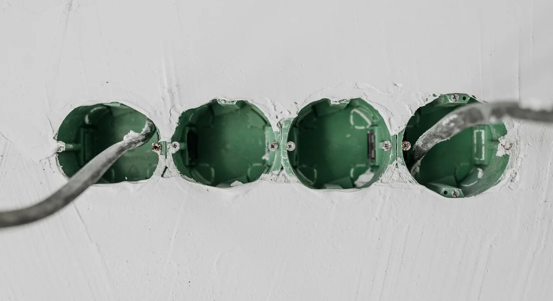 Four green circular electrical boxes embedded in a white wall with a cable entering from the left