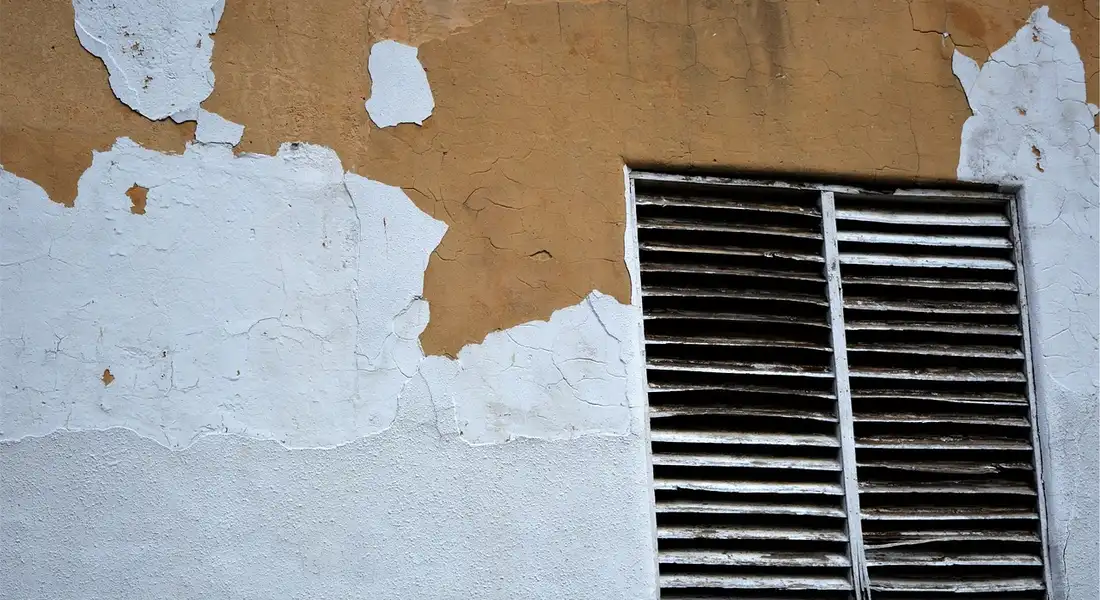 Exterior wall vent grille with peeling paint and weathered surface