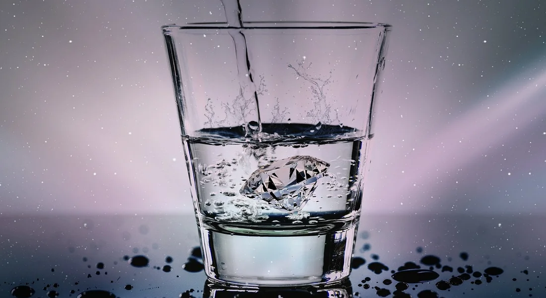 Close-up of a glass of water with splashes and ripples, reflecting light.
