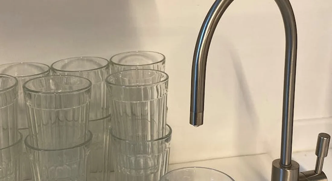 Stacked clear drinking glasses next to a sleek curved kitchen faucet, suggesting water filtration and safe drinking water.