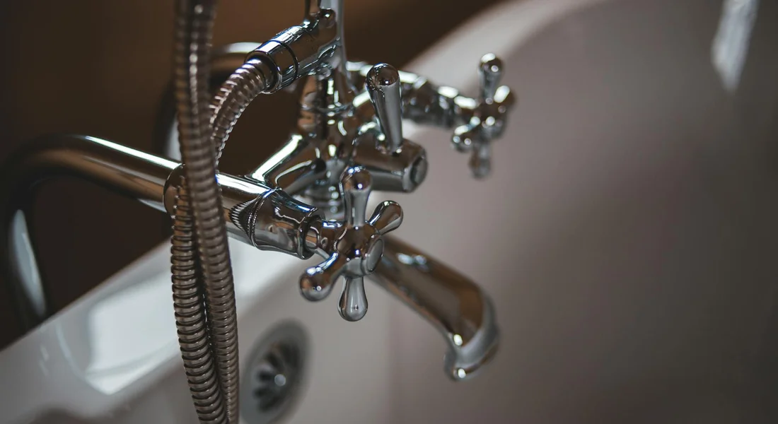 Close-up of a chrome bathroom faucet and plumbing connections, symbolizing sediment buildup in home water lines.