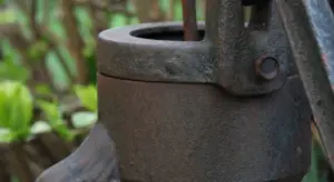 Close-up of a rusty hand water pump mounted on a well housing