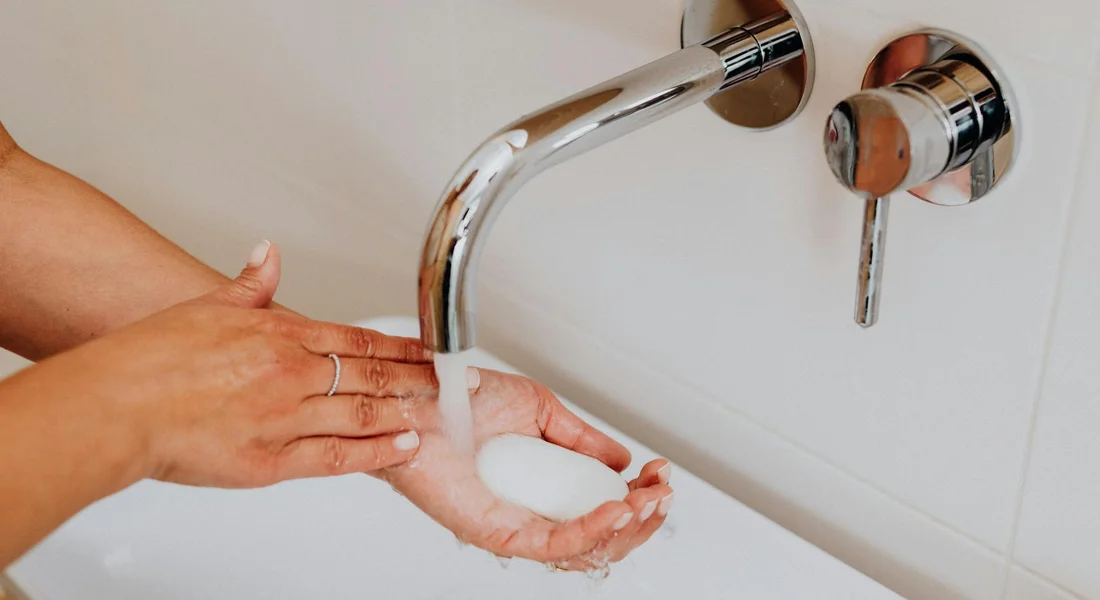 Person's hands lathered with soap under a running faucet in a sink, preparing to begin plumbing work
