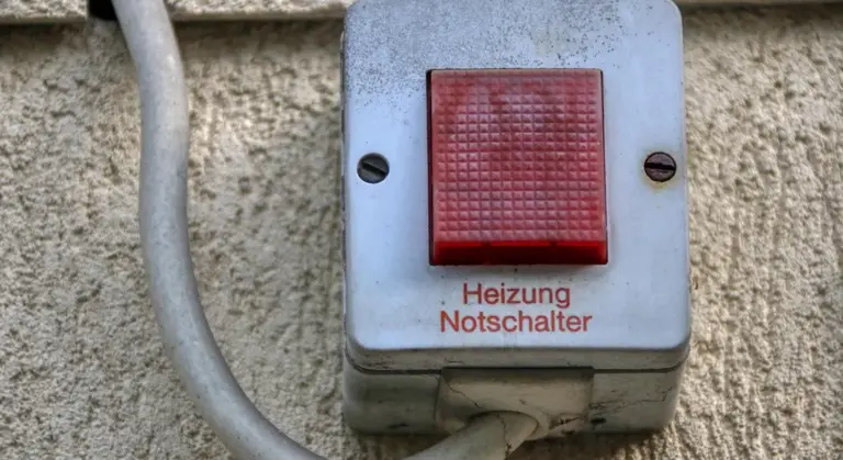 Red push-button emergency shutoff switch labeled 'Heizung Notschalter' mounted on a beige wall