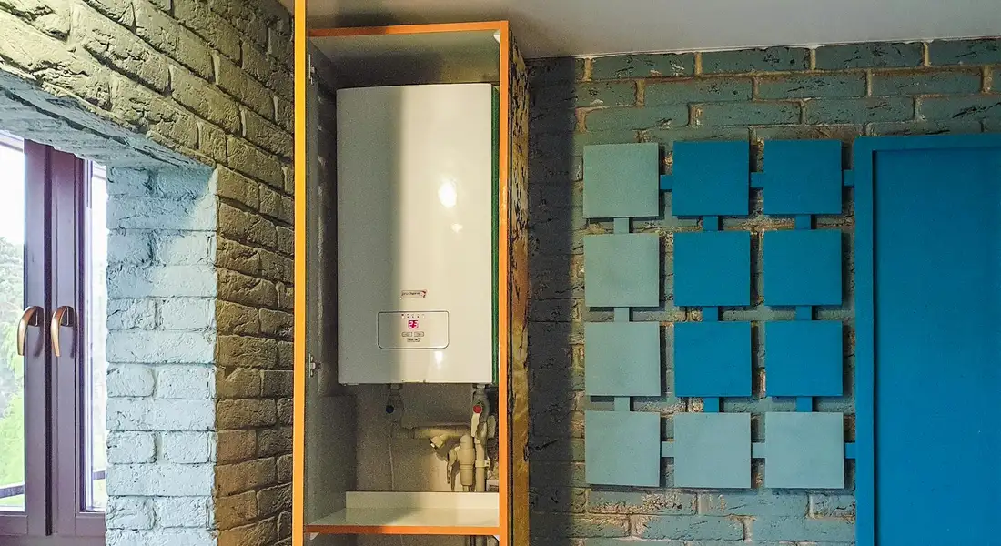 Water heater installed in a recessed cabinet between brick walls with blue tiles; a narrow space around it