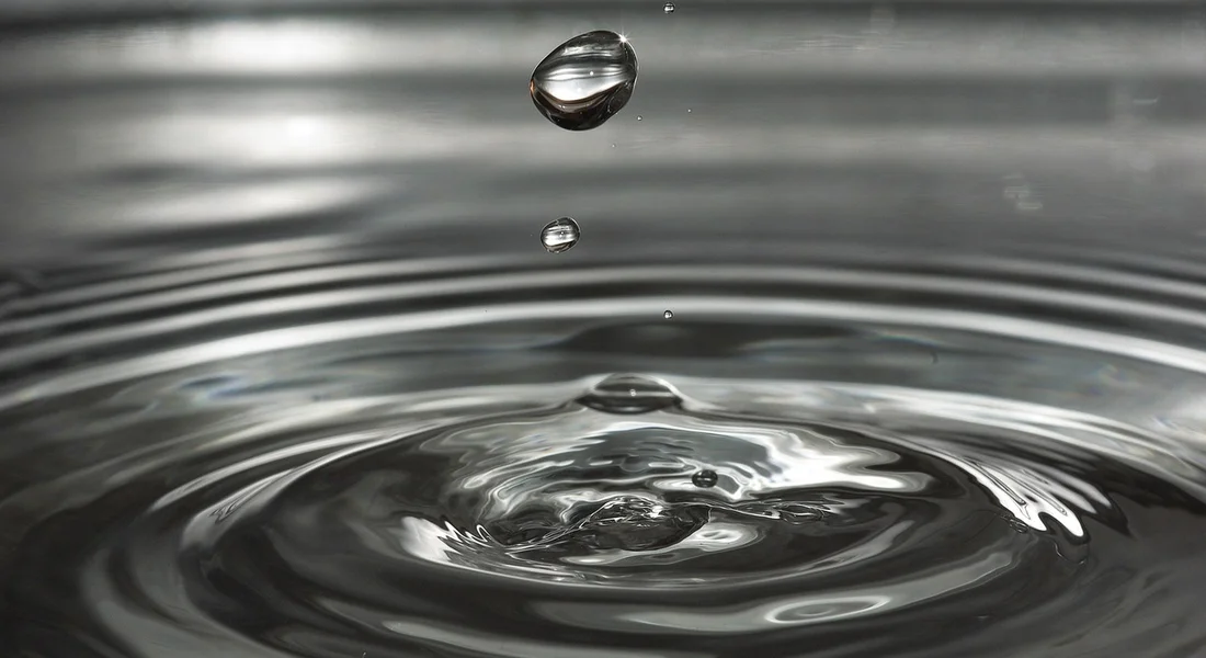 Close-up of a water droplet creating ripples on a smooth water surface, symbolizing ongoing maintenance and monitoring of home water filtration systems.