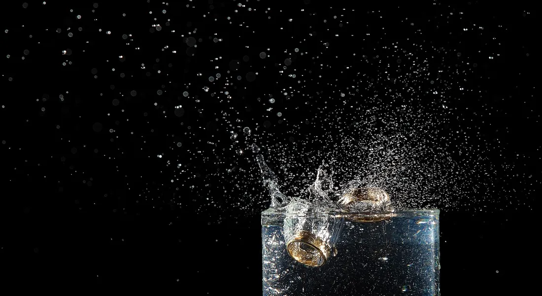 Close-up of a glass with water splashing against a dark background, illustrating hazards associated with drinking hot water.