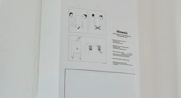 Wall-mounted instruction sign with diagrams and German text 'Hinweis', illustrating maintenance steps and safety cautions for household appliances