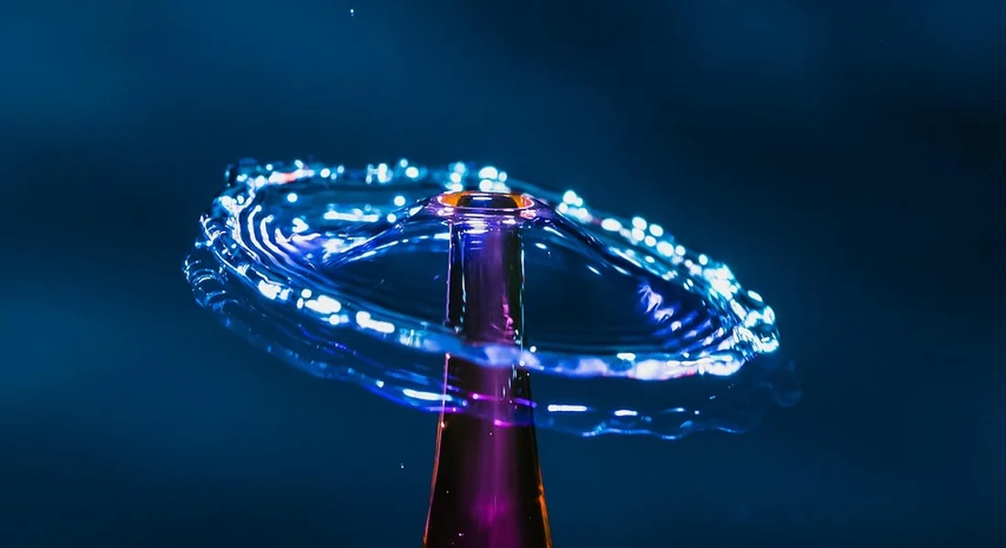 Close-up of a bottle neck with a circular splash of water forming a ring against a blue background.