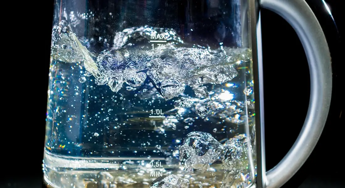 Close-up of a glass electric kettle boiling water with measurement marks visible on the side
