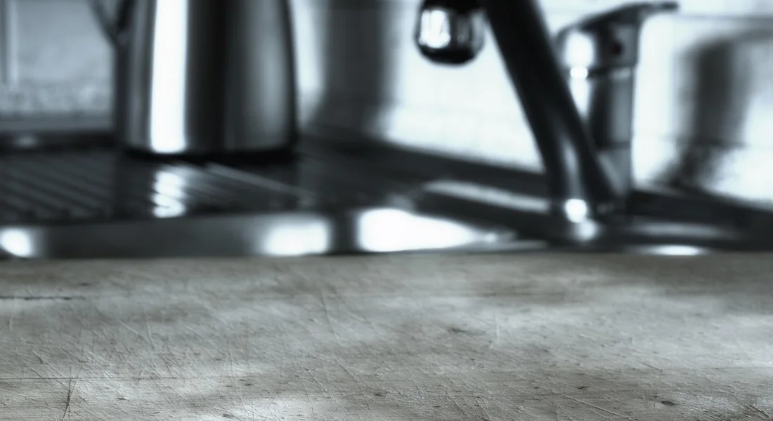 Close-up of a stainless steel kitchen sink and faucet with a concrete countertop, shown in grayscale