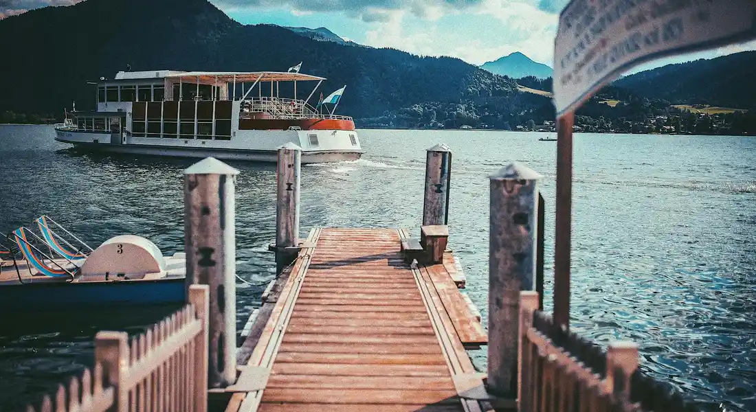 Wooden dock extending into a calm lake with a boat in the background and mountains in the distance