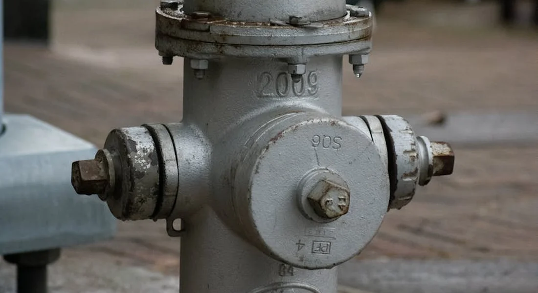 Close-up of a gray metal main water shutoff valve with bolts on the sides, mounted on a water pipe.