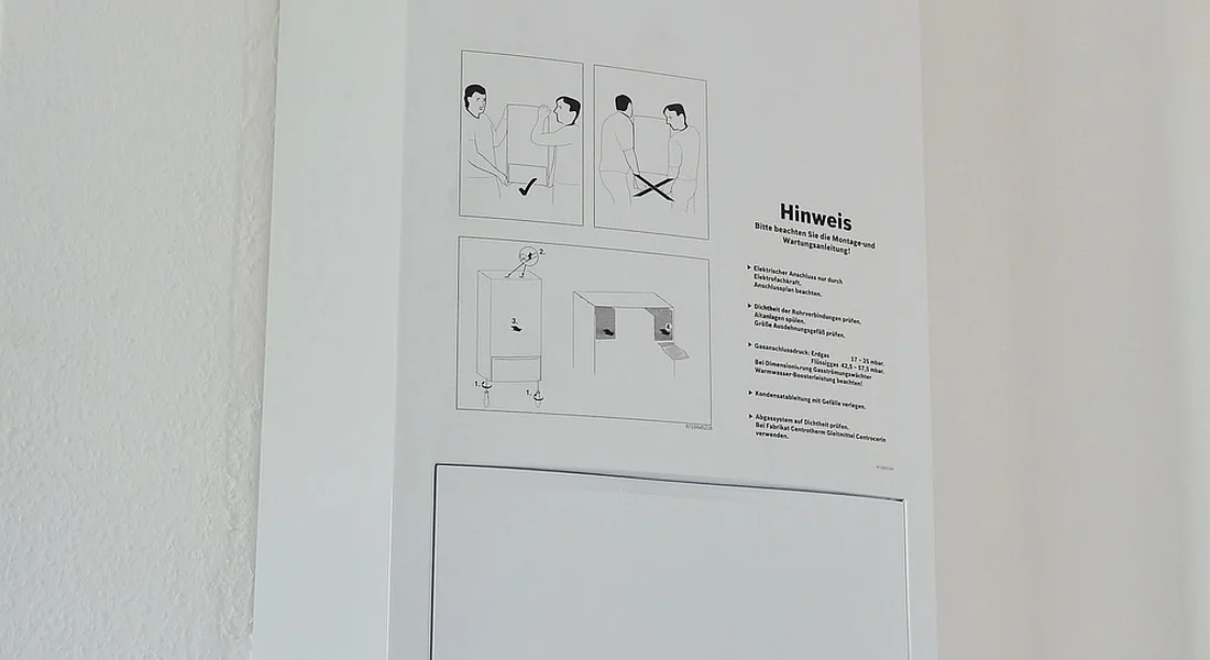 Wall-mounted instruction panel with diagrams and a 'Hinweis' note, illustrating maintenance steps for gas water heaters