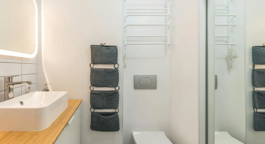 Modern bathroom with a wall-mounted toilet and flush plate, a wooden countertop sink, and a lit mirror—an everyday bathroom scene.