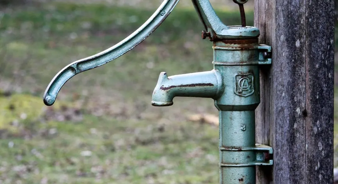 Close-up of an old metal hand water pump mounted on a wooden post