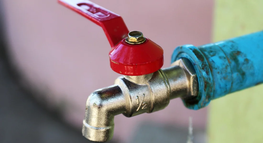 Close-up of an outdoor water faucet with a red lever and blue pipe
