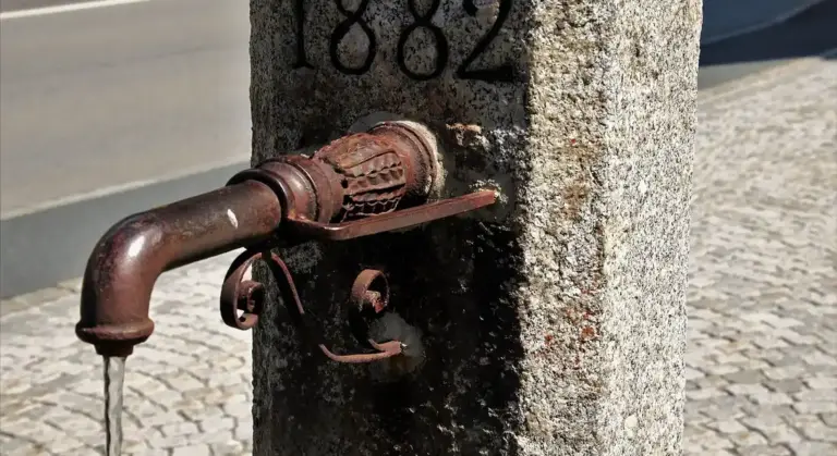 Outdoor water faucet attached to a weathered concrete post with rusted metal components.