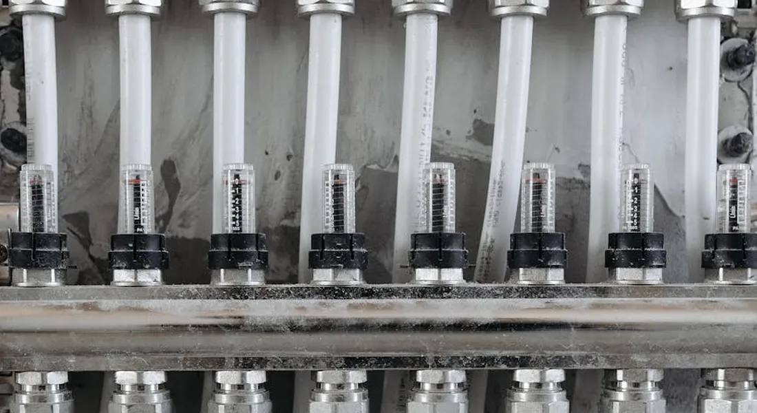Close-up of a PEX plumbing manifold with multiple fittings and crimp rings, showing a dense row of connections that can leak if not installed correctly.