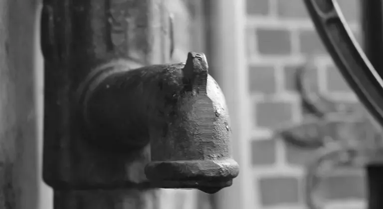 Close-up of a metal pipe valve in a home plumbing setup with a brick wall background, illustrating components of a residential water system.