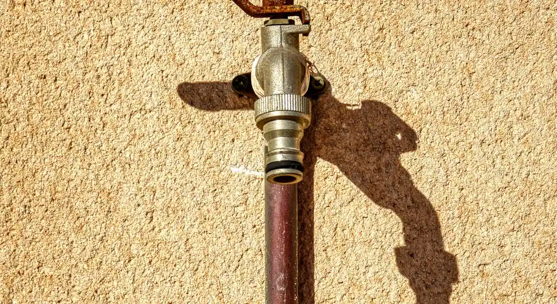 Close-up of a copper water supply line with a shut-off valve mounted on a textured exterior wall; a shadow is cast beside the pipe.