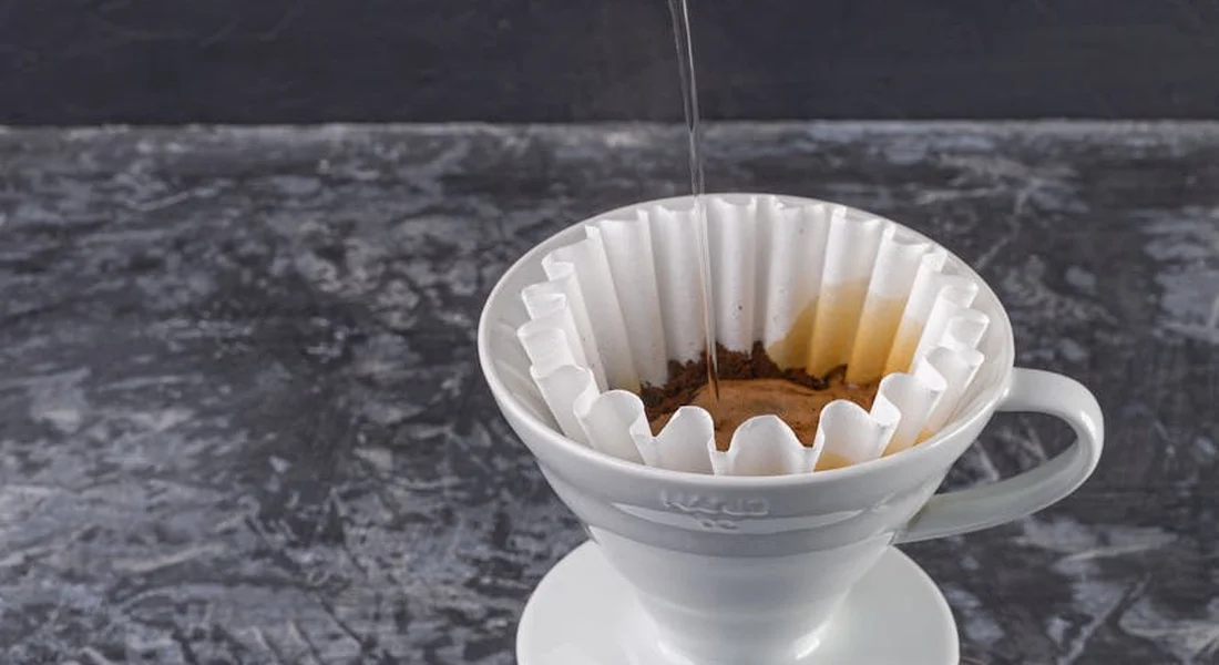 A pour-over coffee maker with a paper filter and coffee grounds on a dark countertop