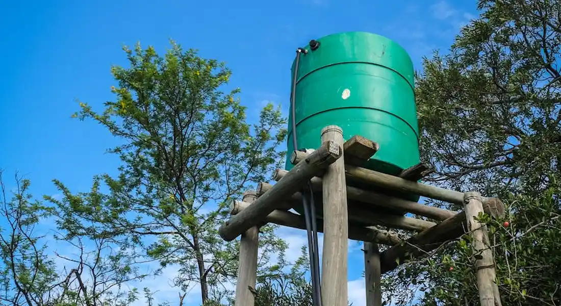 Green vertical pressure tank mounted on a wooden stand outdoors, with trees and blue sky