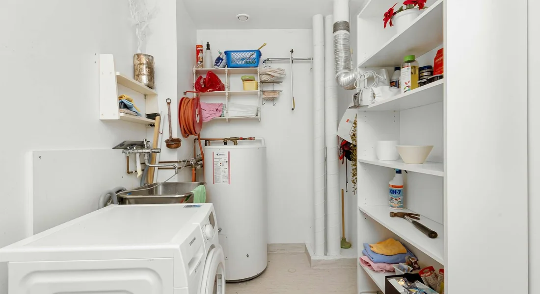 Utility room with a gas-powered water heater, a washing machine, and shelves stocked with cleaning supplies.
