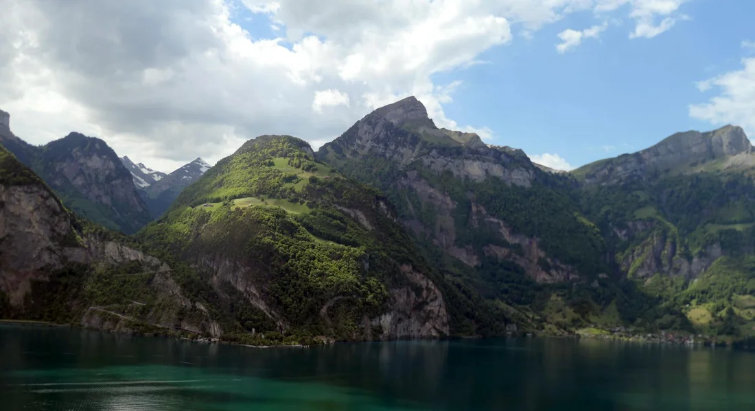 Scenic mountain lake with green hills and a partly cloudy blue sky.
