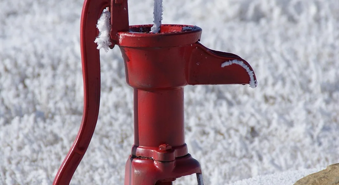 Close-up of a red manual water pump in a snowy outdoor setting, illustrating sump pump issues and alarms