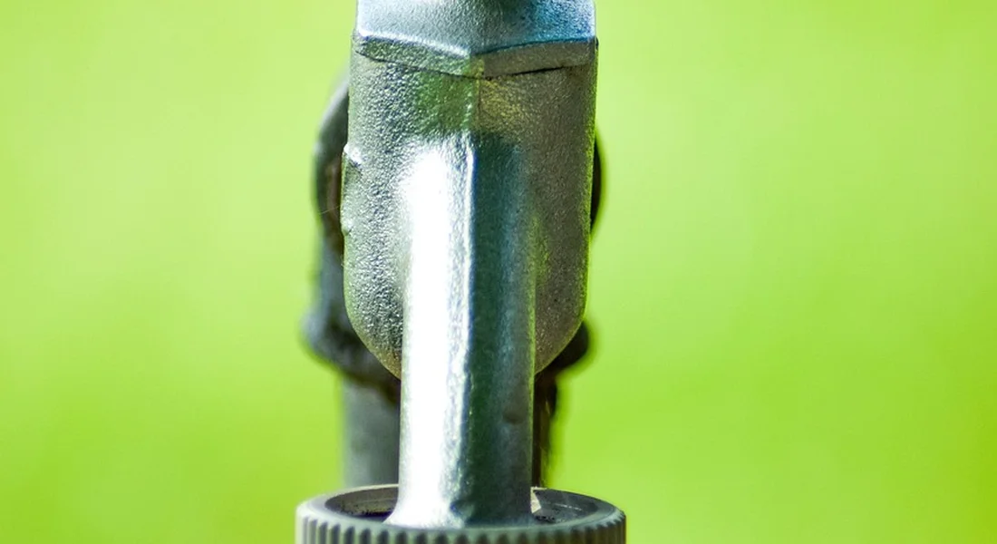 Close-up of a metal valve or nozzle against a bright green background, part of the equipment used to flush refrigerator water lines.