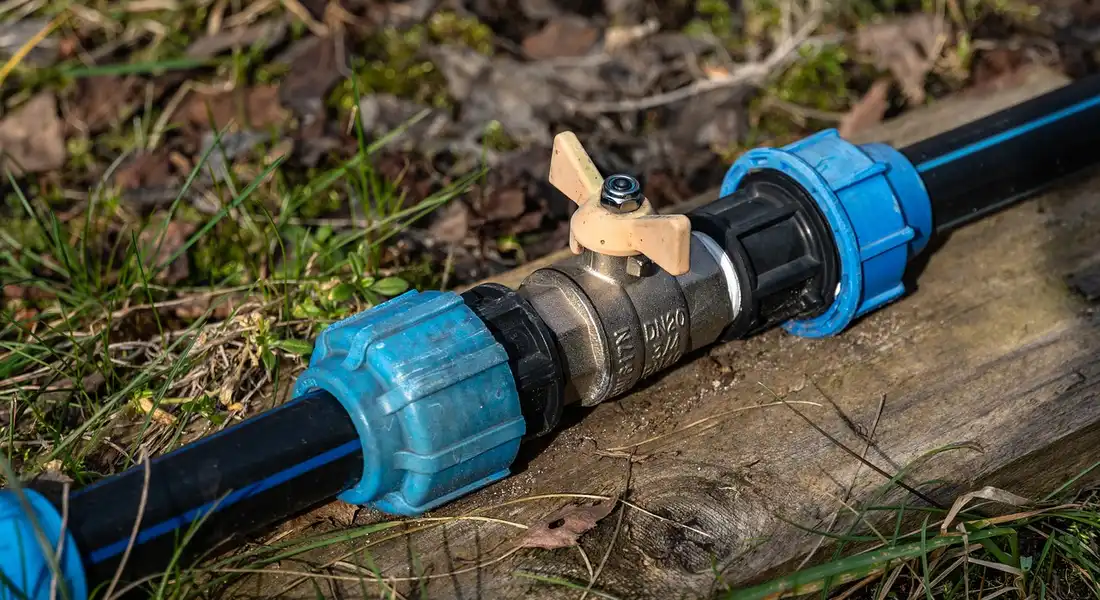 Close-up of a refrigerator water supply line with blue compression fittings and a small brass shut-off valve, laid on a wooden surface outdoors.