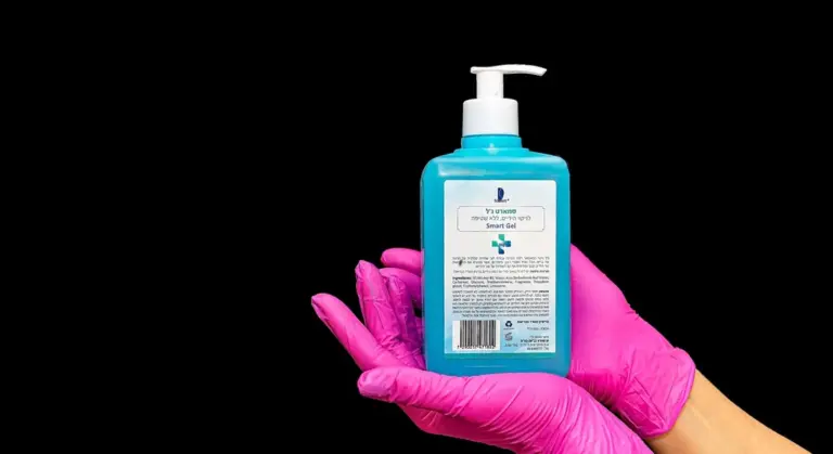 A person wearing bright pink gloves holds a blue bottle of cleaning product against a black background, illustrating the cleaning step for a refrigerator's water dispenser and supply lines.